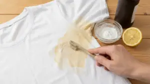 Persona che rimuove una macchia di sudore da una maglietta bianca con spazzolino e rimedi naturali