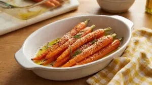 Carote al forno condite con olio, rosmarino e formaggio in una pirofila bianca